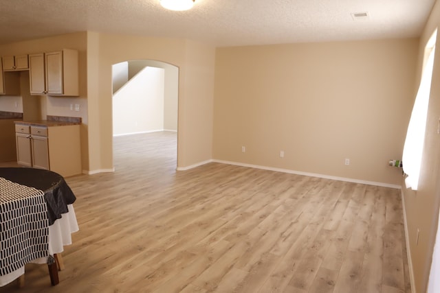 interior space with light wood-style floors, baseboards, arched walkways, and a textured ceiling