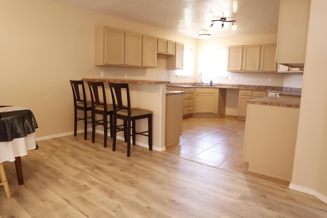 kitchen with cream cabinets, a sink, light wood-style floors, light countertops, and a kitchen bar