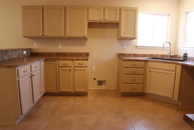 kitchen featuring light tile patterned floors, cream cabinetry, dark countertops, and a sink