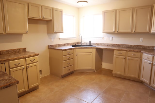 kitchen featuring dark countertops, a sink, cream cabinets, and light tile patterned floors