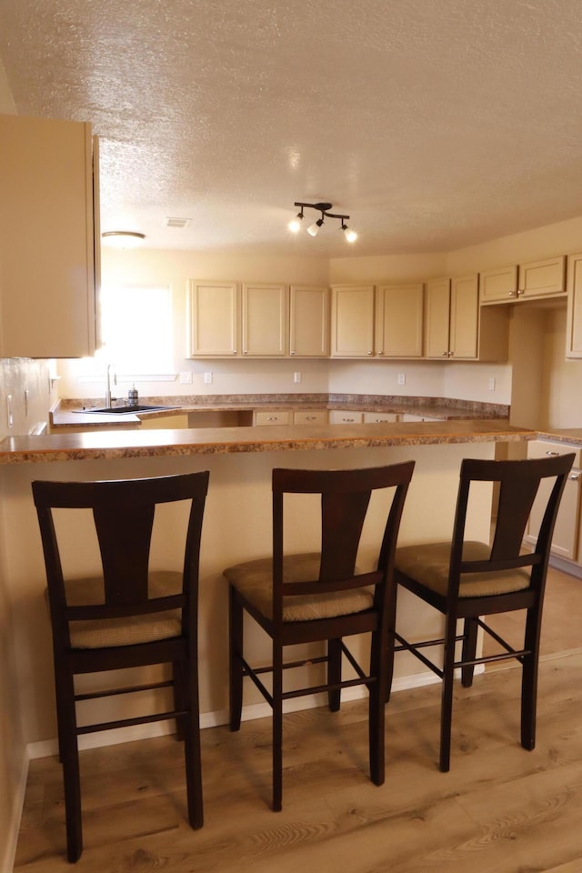 kitchen featuring a textured ceiling, a breakfast bar, light wood-type flooring, and a sink