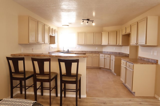 kitchen featuring light tile patterned floors, a textured ceiling, cream cabinets, a sink, and a kitchen bar