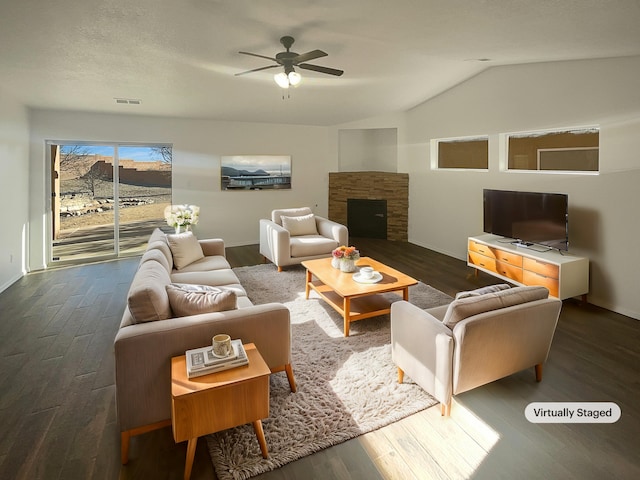 living room featuring lofted ceiling, a fireplace, visible vents, a ceiling fan, and dark wood-style floors