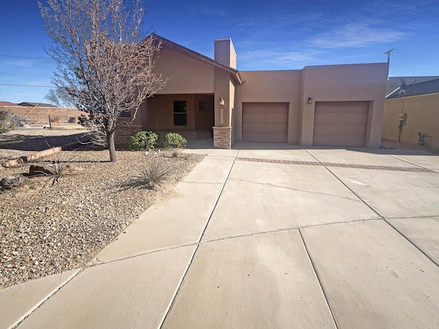 pueblo revival-style home featuring driveway, a chimney, an attached garage, and stucco siding