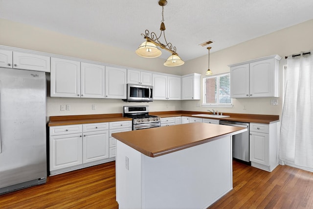 9801 Basha St NW, Albuquerque, NM 87114 - kitchen with appliances with stainless steel finishes, dark wood-style floors, white cabinets, and decorative light fixtures