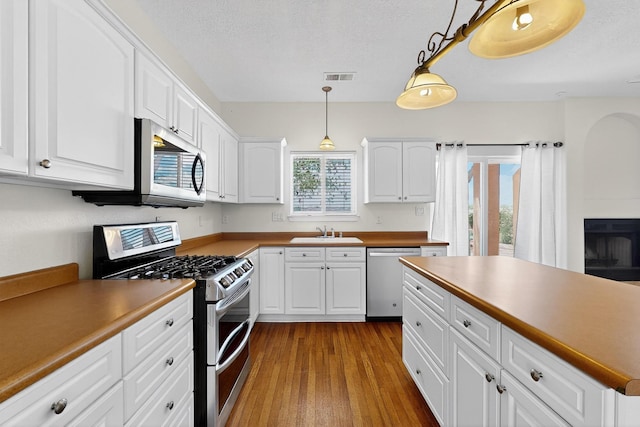 9801 Basha St NW, Albuquerque, NM 87114 - kitchen with appliances with stainless steel finishes, wood finished floors, white cabinets, pendant lighting, and a textured ceiling