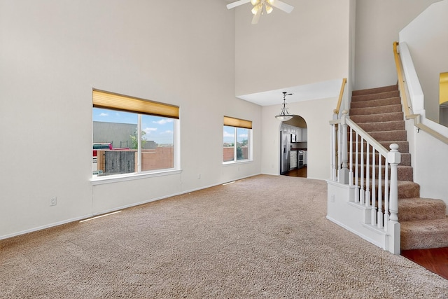9801 Basha St NW, Albuquerque, NM 87114 - unfurnished living room featuring arched walkways, a ceiling fan, carpet floors, stairway, and a towering ceiling