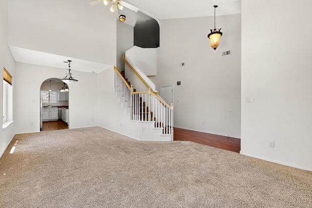 9801 Basha St NW, Albuquerque, NM 87114 - unfurnished living room with carpet flooring, a ceiling fan, a high ceiling, stairs, and arched walkways
