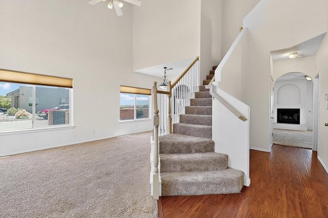 9801 Basha St NW, Albuquerque, NM 87114 - staircase with a high ceiling, ceiling fan, a fireplace with raised hearth, wood finished floors, and arched walkways