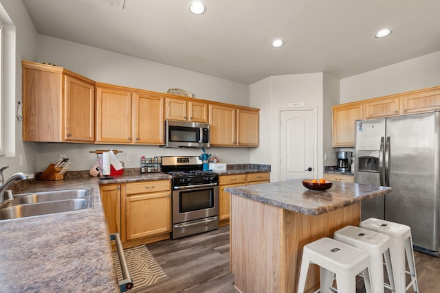 kitchen with dark wood-style floors, appliances with stainless steel finishes, a breakfast bar, a center island, and a sink