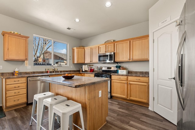 kitchen with a kitchen island, visible vents, appliances with stainless steel finishes, dark countertops, and a kitchen bar