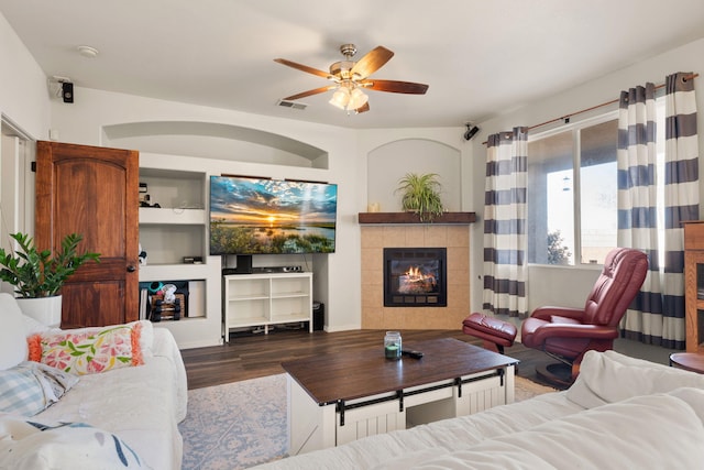 living room featuring a ceiling fan, a fireplace, visible vents, and dark wood-style flooring