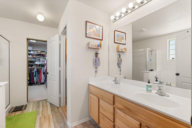 bathroom featuring a stall shower, a walk in closet, a sink, and wood finished floors