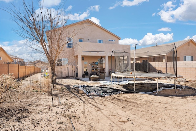 back of property with a trampoline, a fenced backyard, and stucco siding