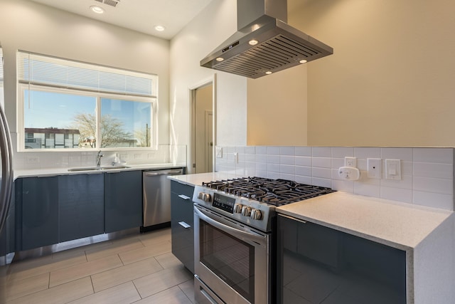 kitchen with tasteful backsplash, island range hood, appliances with stainless steel finishes, light countertops, and a sink