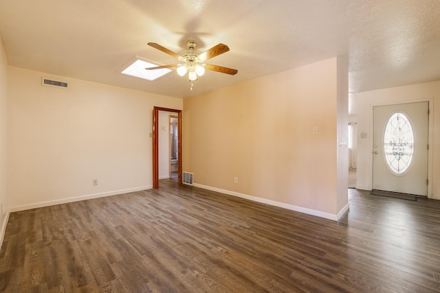 interior space with dark wood-style floors, ceiling fan, a skylight, and visible vents