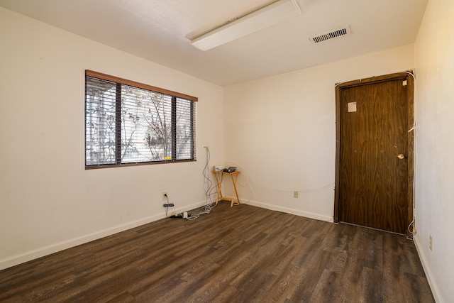 unfurnished room with dark wood-type flooring, visible vents, and baseboards