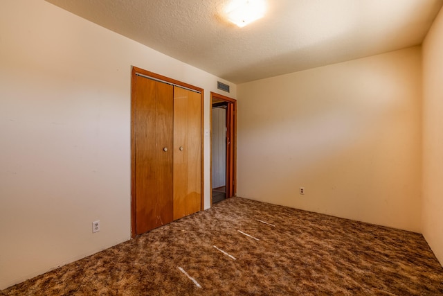 unfurnished bedroom featuring carpet floors, a textured ceiling, visible vents, and a closet