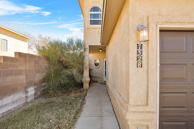 doorway to property featuring a garage, fence, and stucco siding