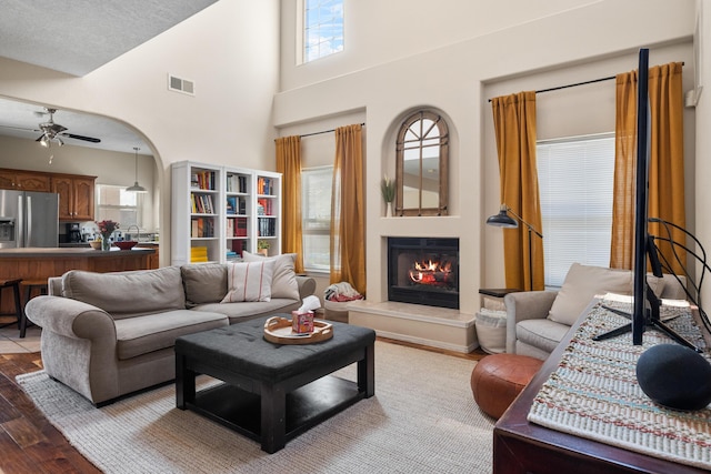 living room featuring a warm lit fireplace, visible vents, arched walkways, a ceiling fan, and wood finished floors