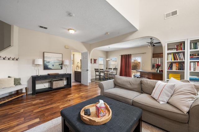 living area featuring a textured ceiling, dark wood finished floors, visible vents, and a ceiling fan