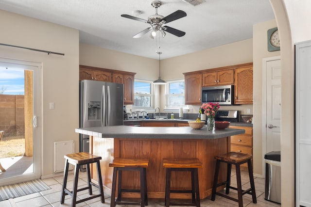 kitchen featuring a kitchen breakfast bar, stainless steel appliances, dark countertops, and brown cabinets