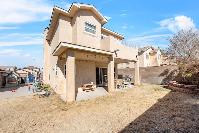 rear view of house featuring a fenced backyard, a balcony, a residential view, stucco siding, and a patio area