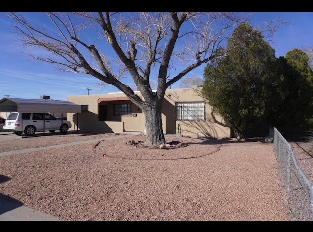 view of front of home with fence, a detached carport, and stucco siding