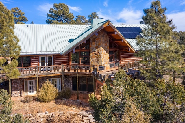 rear view of property featuring stone siding, a chimney, metal roof, a standing seam roof, and roof mounted solar panels