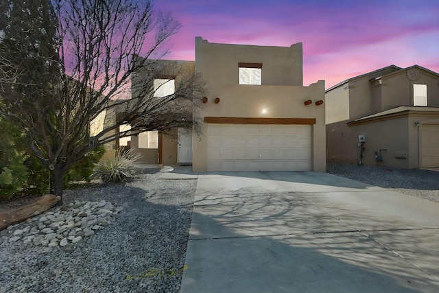 pueblo-style home with a garage, driveway, and stucco siding