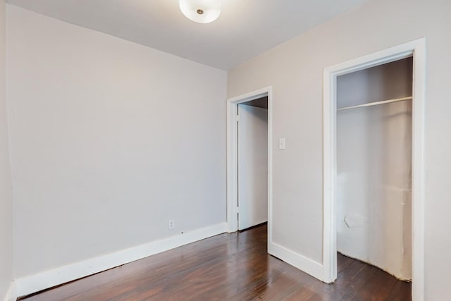 unfurnished bedroom with a closet, baseboards, and dark wood-type flooring