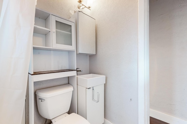 bathroom featuring toilet, a textured wall, and a sink