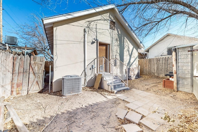 rear view of house with fence, central AC unit, and stucco siding