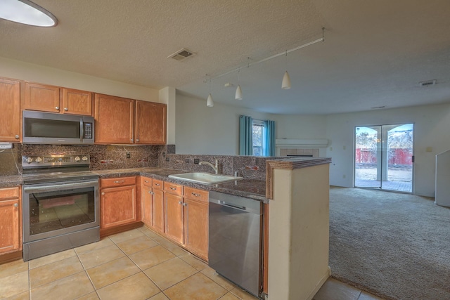 kitchen with dark countertops, open floor plan, a peninsula, stainless steel appliances, and a sink