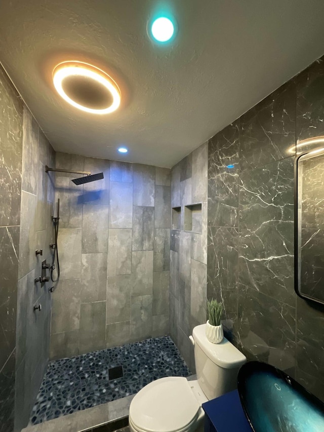 bathroom with tiled shower, recessed lighting, toilet, and tile walls