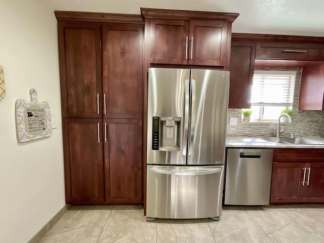 kitchen with a sink, baseboards, light countertops, appliances with stainless steel finishes, and decorative backsplash