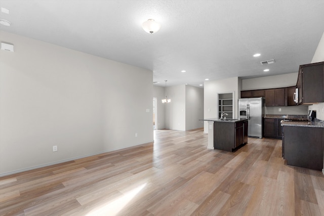 kitchen with visible vents, hanging light fixtures, open floor plan, an island with sink, and stainless steel fridge with ice dispenser