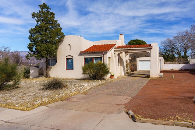 pueblo revival-style home featuring a tile roof, driveway, a chimney, and stucco siding