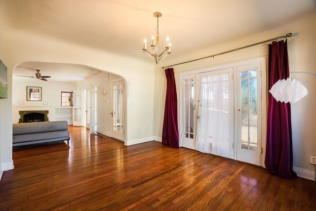 foyer with arched walkways, ceiling fan with notable chandelier, a fireplace, and dark wood finished floors