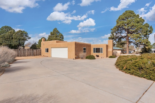 pueblo revival-style home featuring driveway, a garage, a chimney, and stucco siding