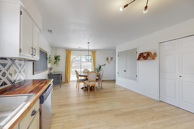 kitchen featuring visible vents, light wood-style flooring, stainless steel dishwasher, white cabinetry, and a sink