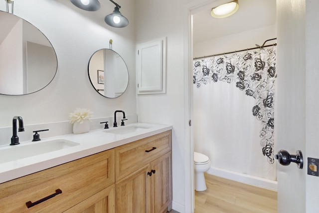 full bath featuring double vanity, a sink, toilet, and wood finished floors