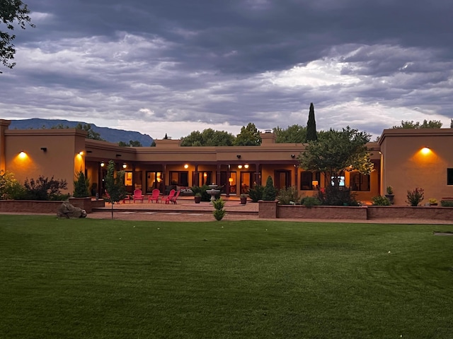 back of house featuring a patio area, a lawn, a mountain view, and stucco siding