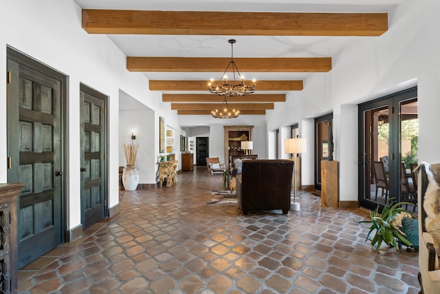 foyer entrance featuring a chandelier, beam ceiling, baseboards, and stone tile floors