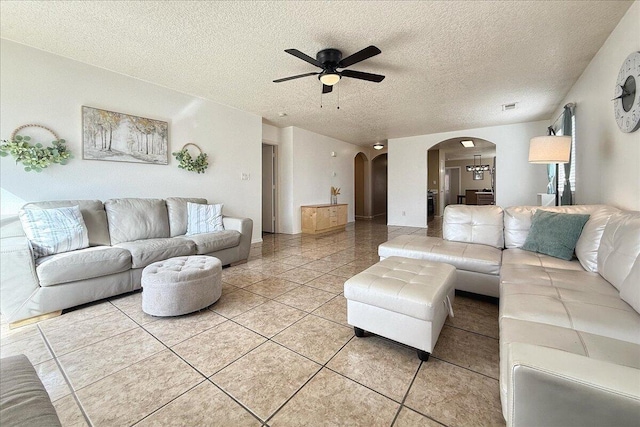 living room featuring arched walkways, light tile patterned floors, a textured ceiling, a ceiling fan, and visible vents