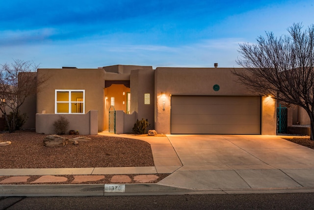 pueblo revival-style home with concrete driveway, an attached garage, and stucco siding