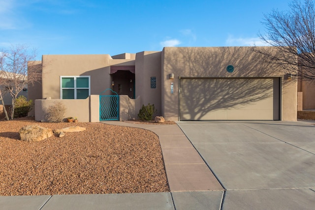 pueblo revival-style home featuring a garage, concrete driveway, and stucco siding