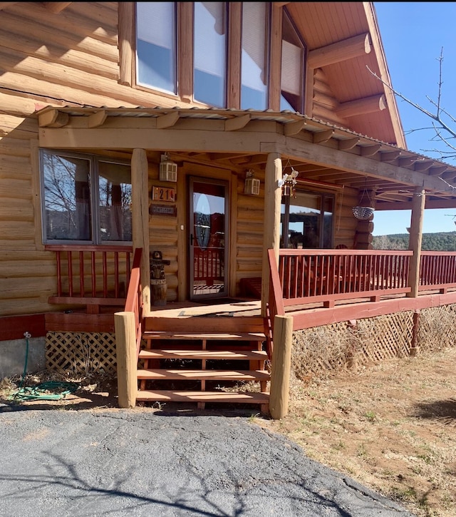 view of exterior entry featuring covered porch and log siding