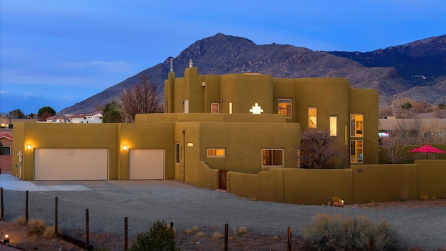 southwest-style home with a fenced front yard, an attached garage, a mountain view, and stucco siding