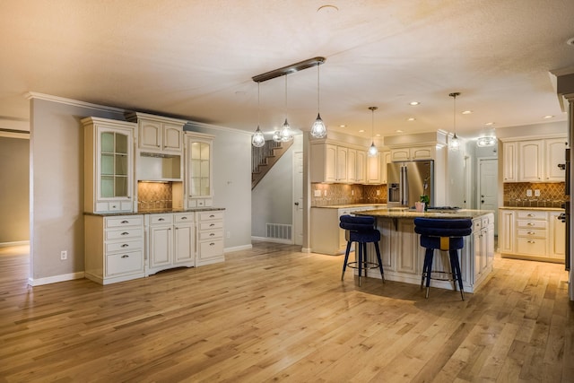 kitchen with a breakfast bar area, stainless steel refrigerator with ice dispenser, an island with sink, glass insert cabinets, and pendant lighting